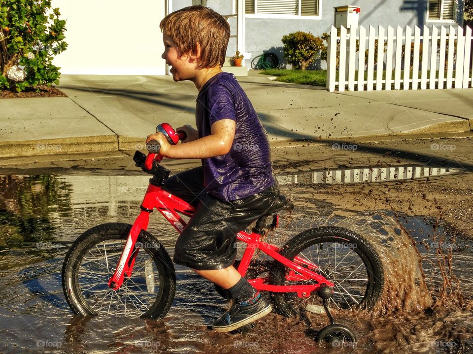 Boy Riding Bike Through Puddle