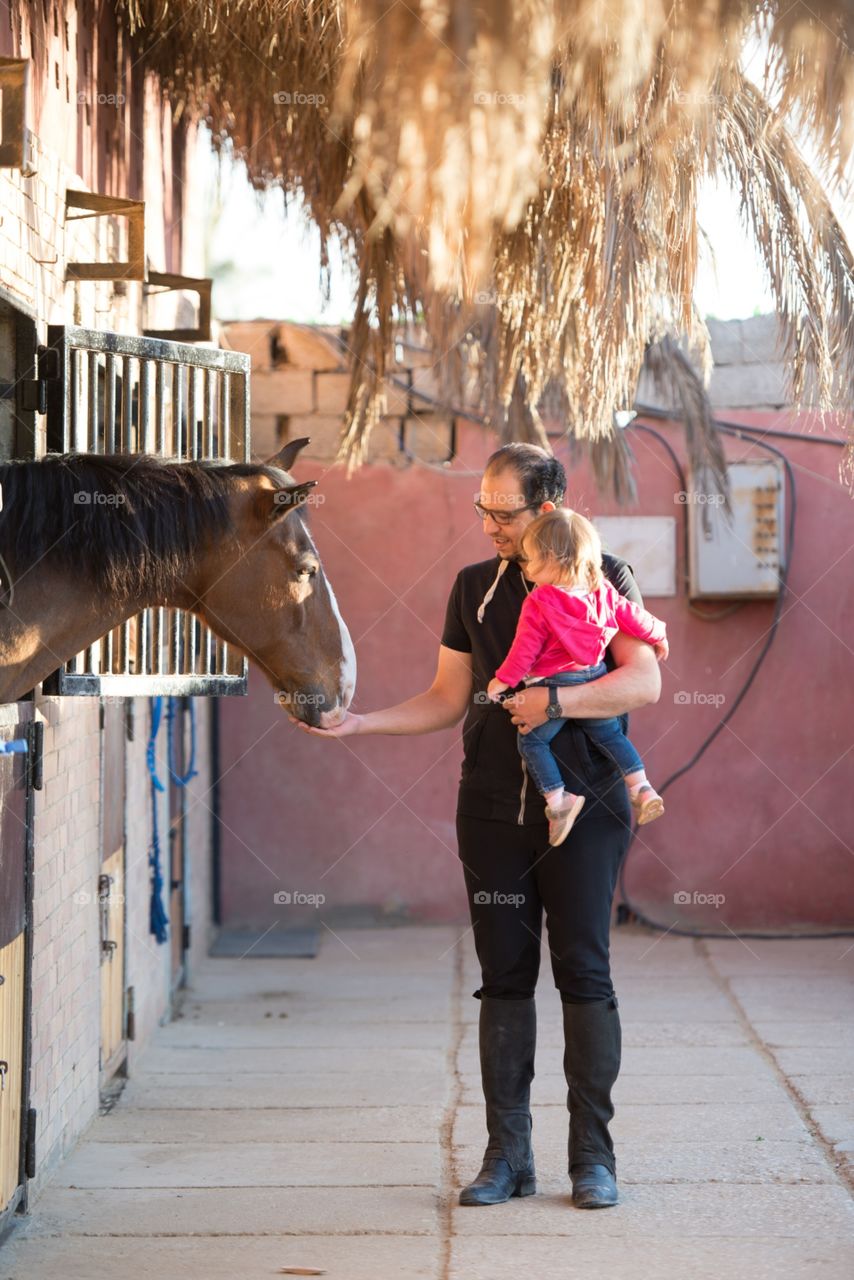 a father holding his daughter and feeding the horse