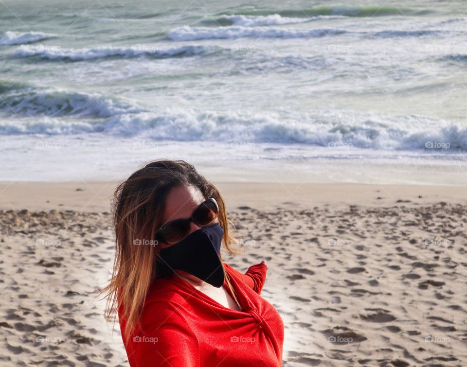 Woman wearing red dress and mask on the beach 