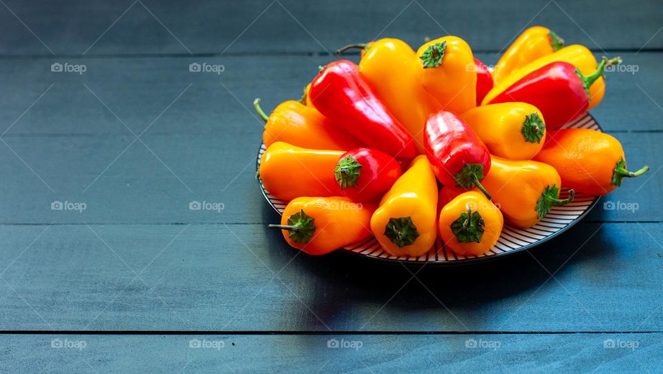 A plate of sweet,colorful peppers on a black wooden table,closeup.