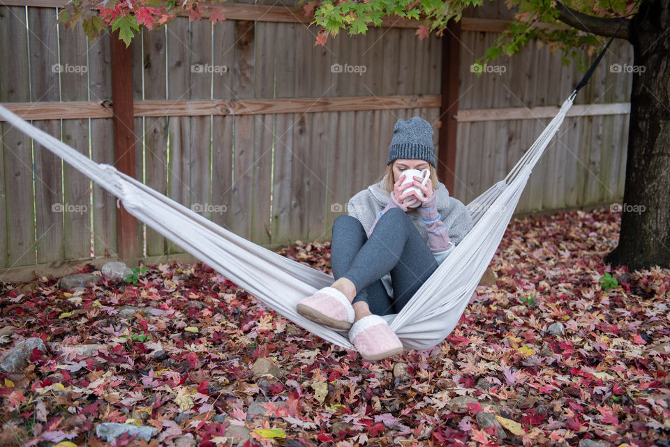 Young millennial woman sipping coffee in a hammock outdoors in the fall