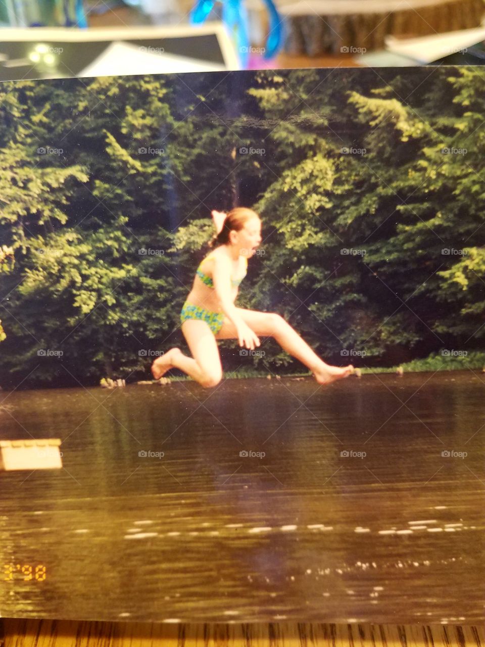 Young redheaded girl running off a dock, jumping into a lake.