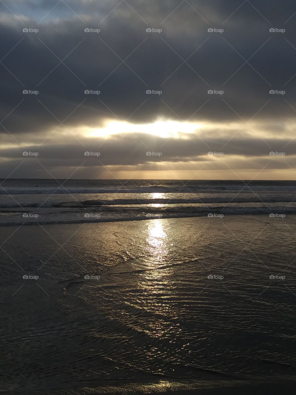 sun rays peering through clouds cascading over waves and sand