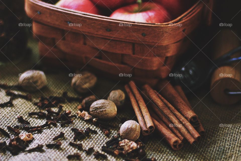 Cinnamon sticks, whole nutmeg, whole cloves, a vintage pie crust crimper, a wooden pastry roller and apples in a basket on burlap