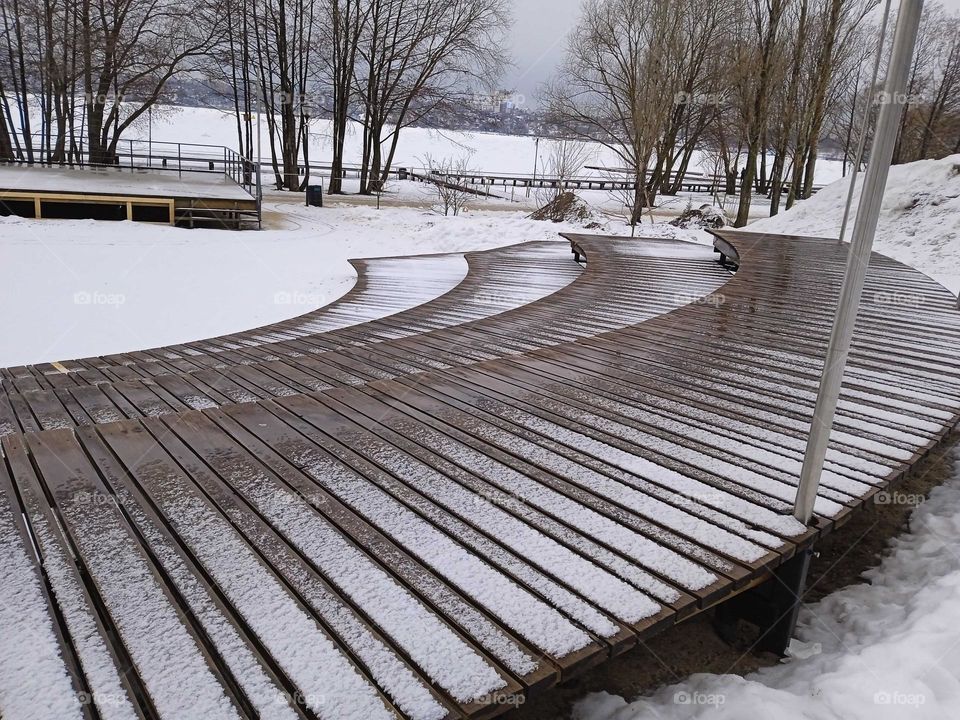 February, gloomy day, walking park near the river, seats covered with snow