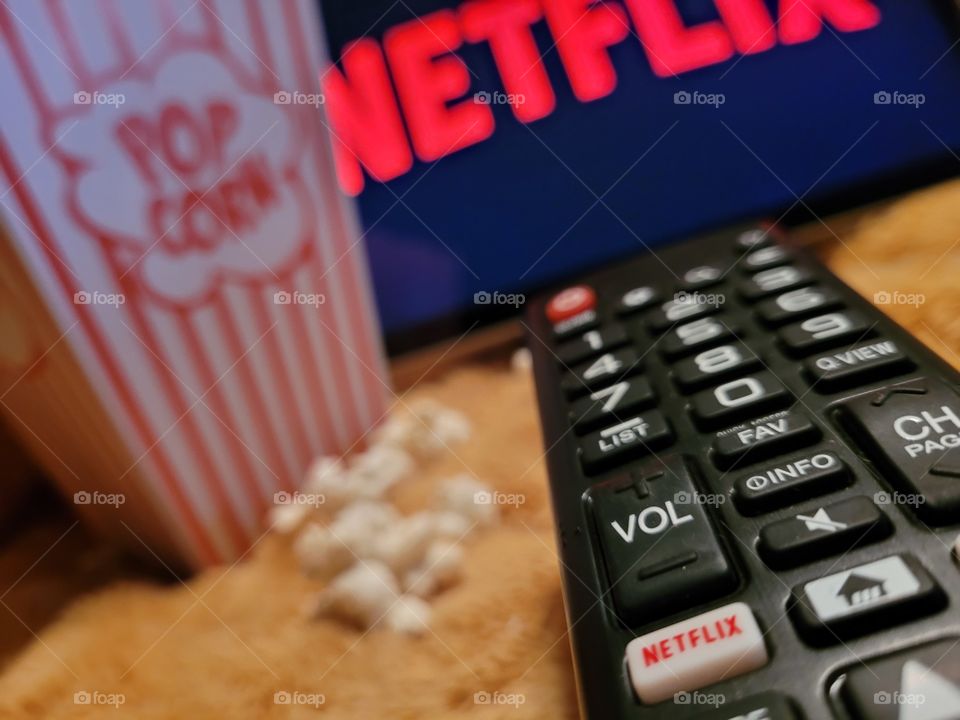 Aiming the remote control at television screen to choose favorite netflix channel to binge watch TV shows or movies for a fun and cozy night in with a popcorn snack