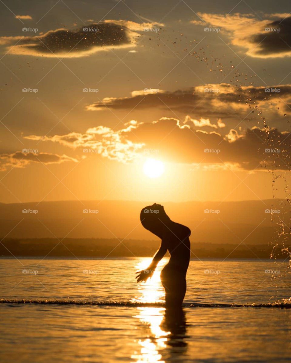 The body of a girl in the sea water as if she spouts the flame of the sun from her mouth