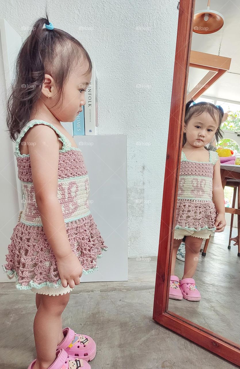 A little girl looks standing in front of a mirror while looking at the sad toward the mirror