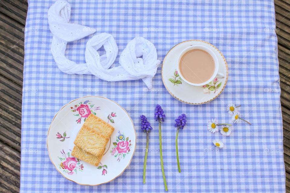A cup Of tea and biscuits on a blue gingham tablecloth 