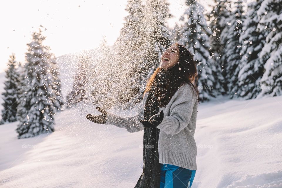 Happy woman playing in the snow, while surrounded by a beautiful snowy landscape.