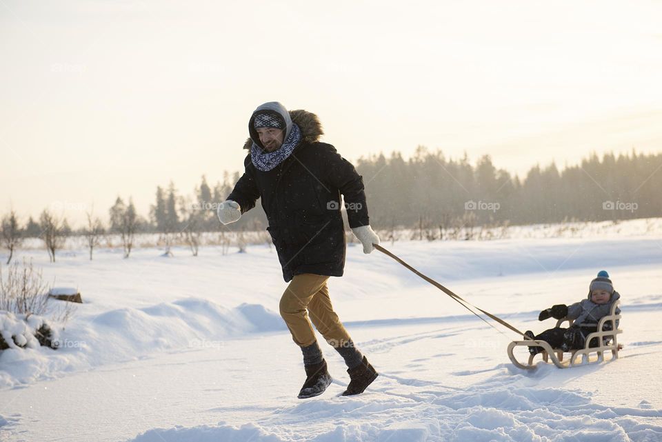 Dad and baby boy rides sled on the ice of a frozen lake