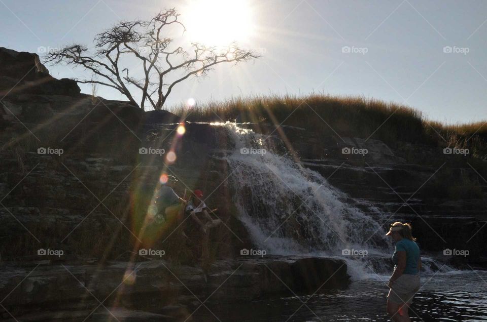 Silhouette of tree above waterfall in rural KZN South Africa with sun shining from behind