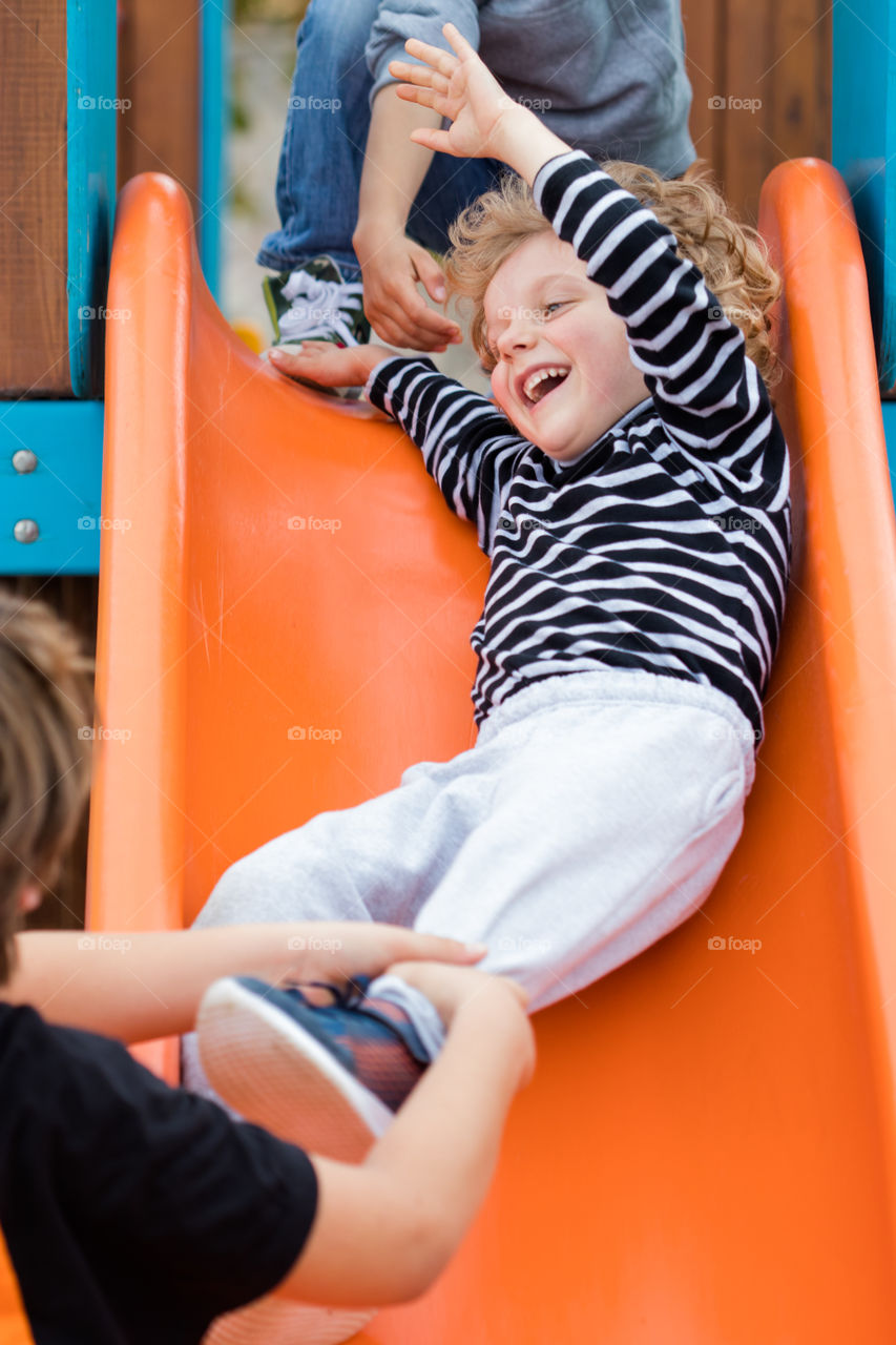 a blond boy coming down an orange slide lauthing