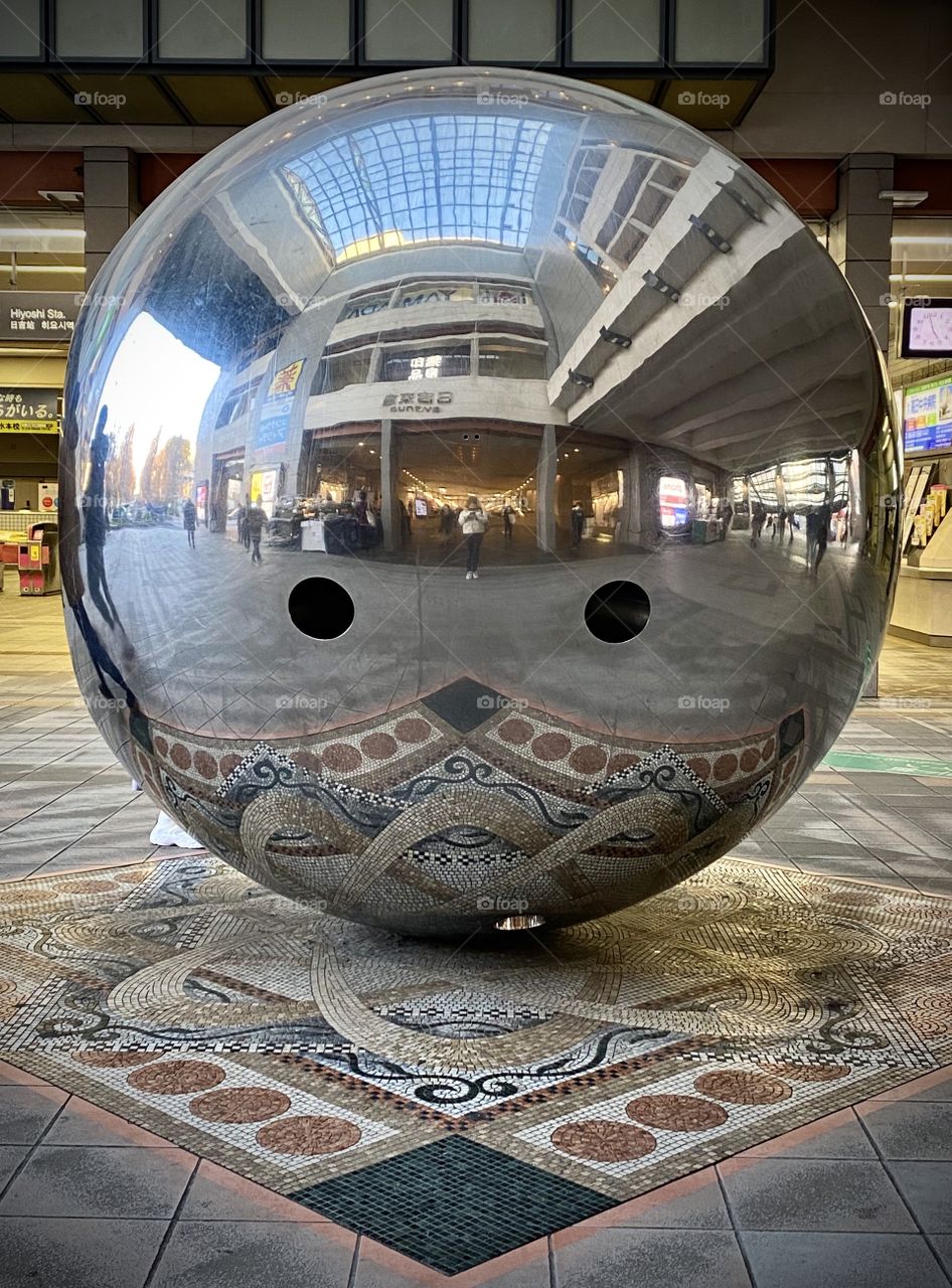Large metallic reflective-mirrored spherical object outside a train station in Japan. 