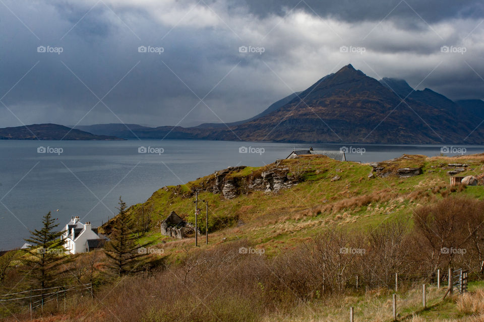 Dramatic rain clouds move inland towards the Cuillin Mountains on the Isle of Skye. A cottage on a grassy heathland is in the foreground
