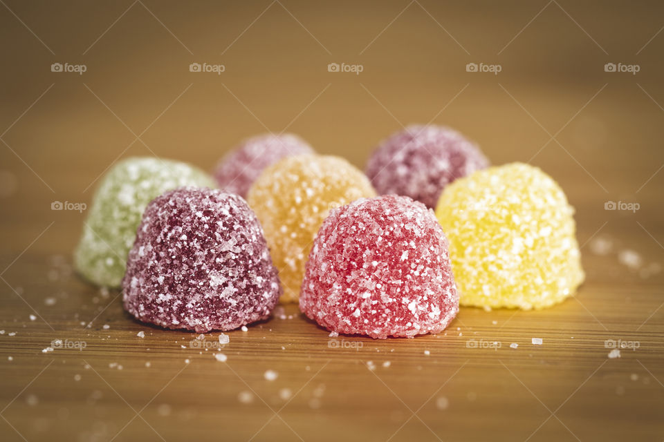 A macro portrait of seven colorful sugar coated pieces of candy on a wooden table with some sugar lying around them.