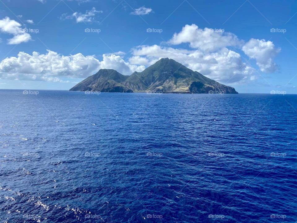 The mountains in the distance are the perfect match to the sapphire blue waters of this beautiful island. The sky is a beautiful light blue with welcoming white clouds. 