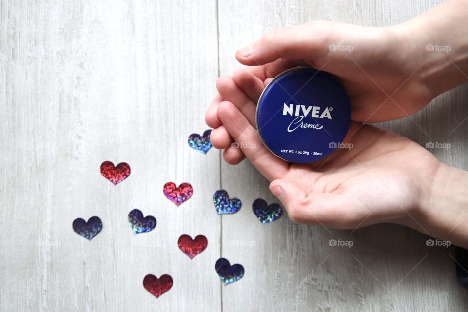 Hands holding Nivea crème product with hearts flat lay 