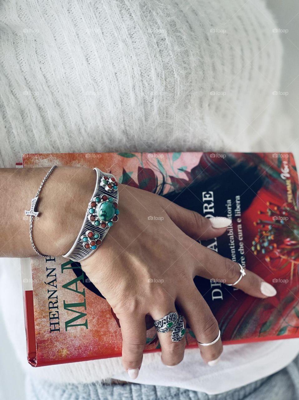 Woman’s hand wearing silver bracelets, silver rings and white nail polish holding a book 