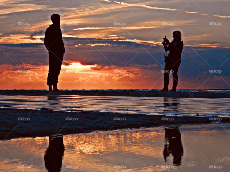 World of silhouettes and shadows - A couple frolic in the magnificent sunset as they take photos while wading in the in the Gulf of Mexico. They reflect from the descending sunset