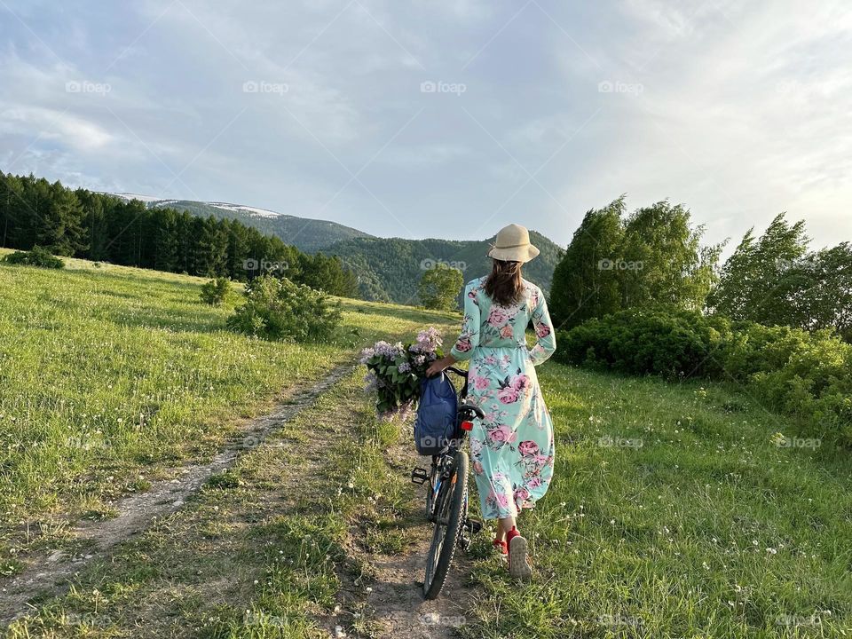 Girl in a dress with lilacs on a bicycle