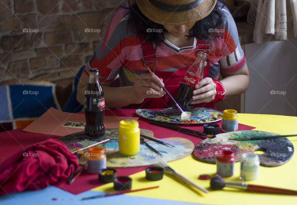 A woman painting on the table, colorful workplace, Coca-Cola bottles on the table