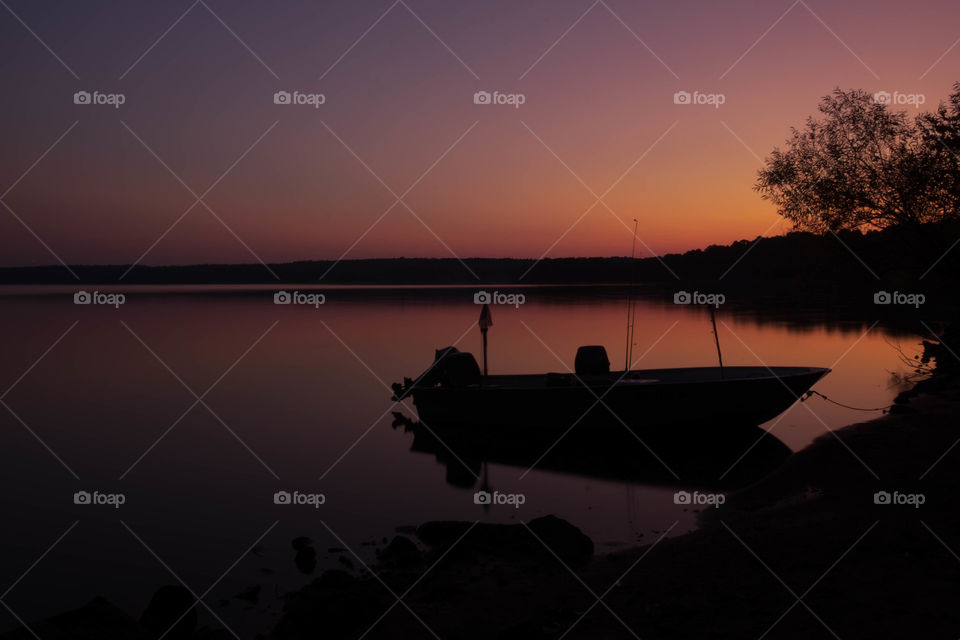 A tied boat floats perfectly still during the vivid twilight period just before sunrise. Rollingview State Park near Raleigh North Carolina. 