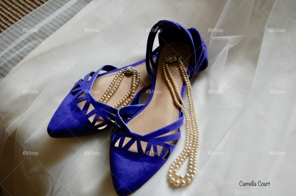 Beautiful pair of blue suede flats with pearl necklaces on a bridal veil