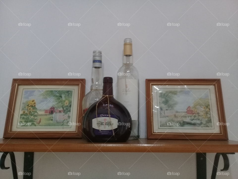 imágenes de botellas de vidrio y cuadros a ambos lados sobre una repisa de madera lustrada