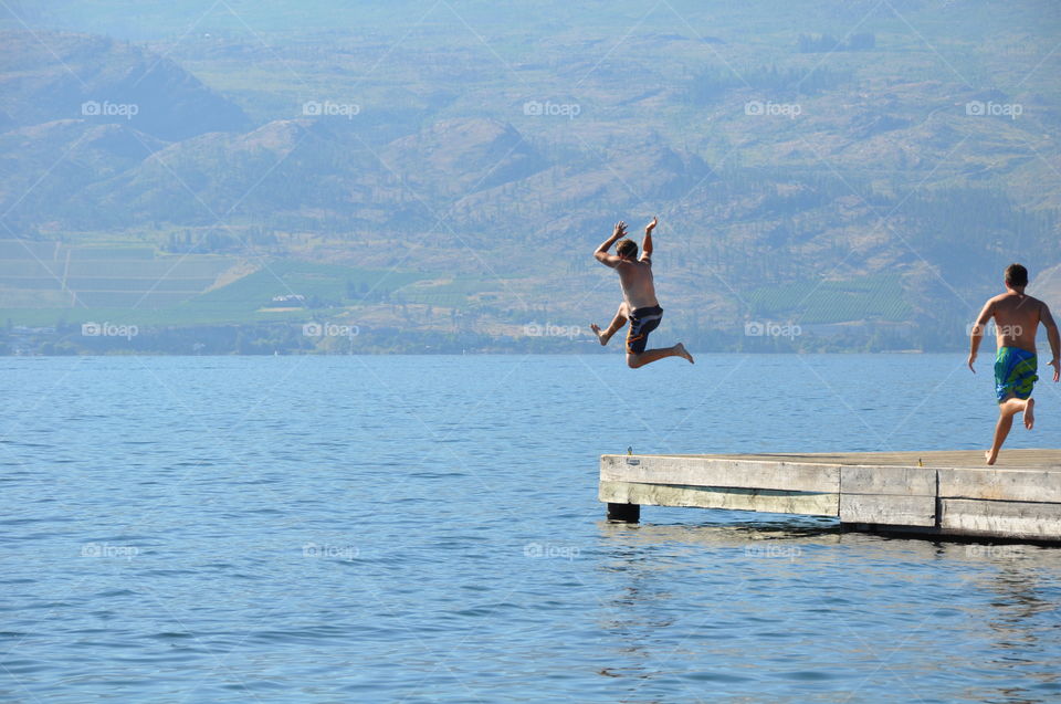 Young male jumping into lake off dock