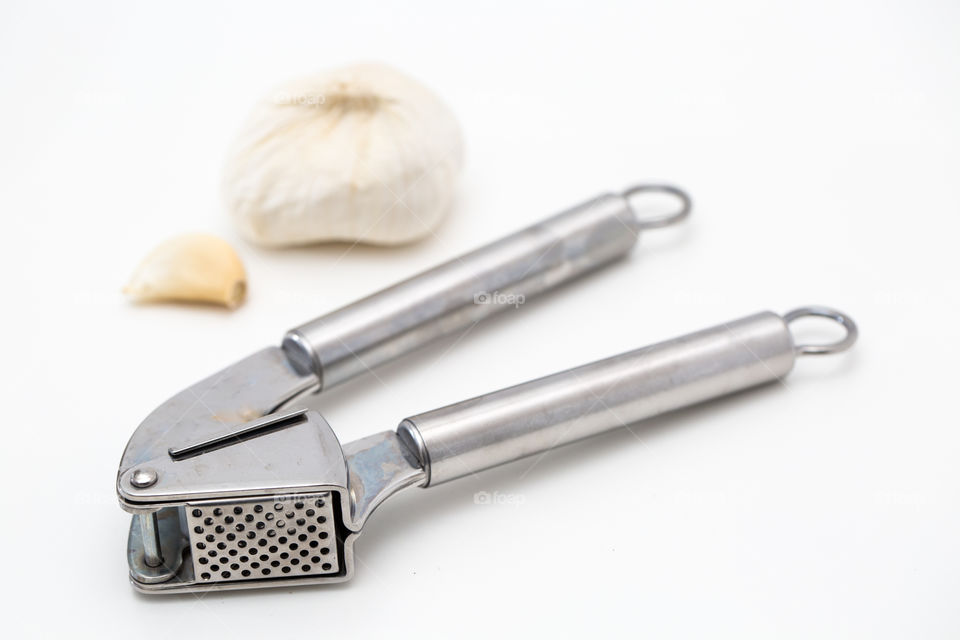 Product kitchen utensil - garlic press with garlic on pure white background. Stainless steel.