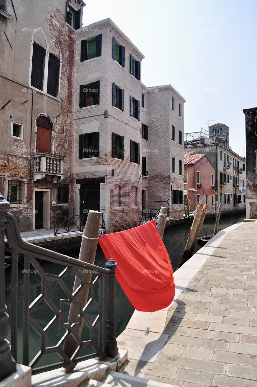 Red bed sheet hung out to dry in the sun in a street in Venice