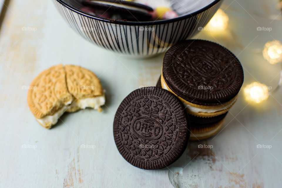 Stack of thin Oreo with cinnamon Oreos on rustic wood with striped bowl and lights in background and cinnamon Oreo with bite 