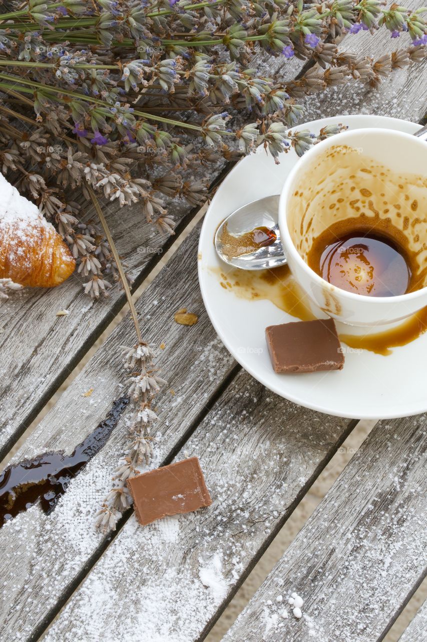 Empty coffee cup, pieces of milk chocolate, sugar powder, croissant on a wooden surface. High angle shot.