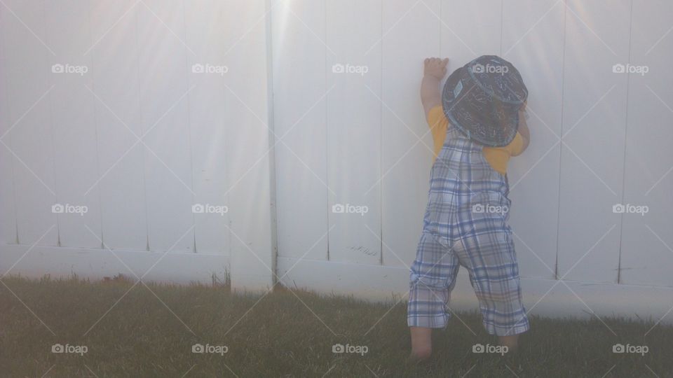 Baby boy walking along a white fence