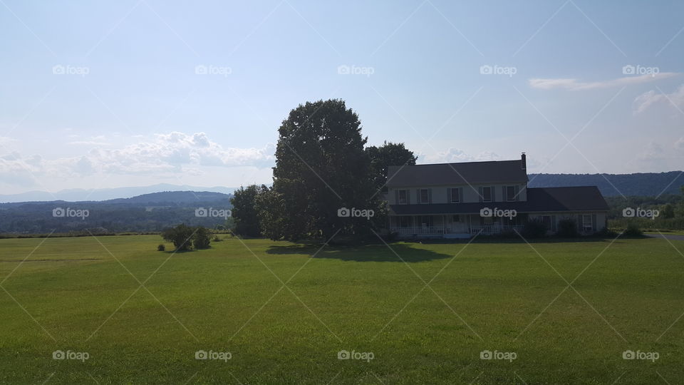 farmhouse in a meadow with trees and mountains in the background