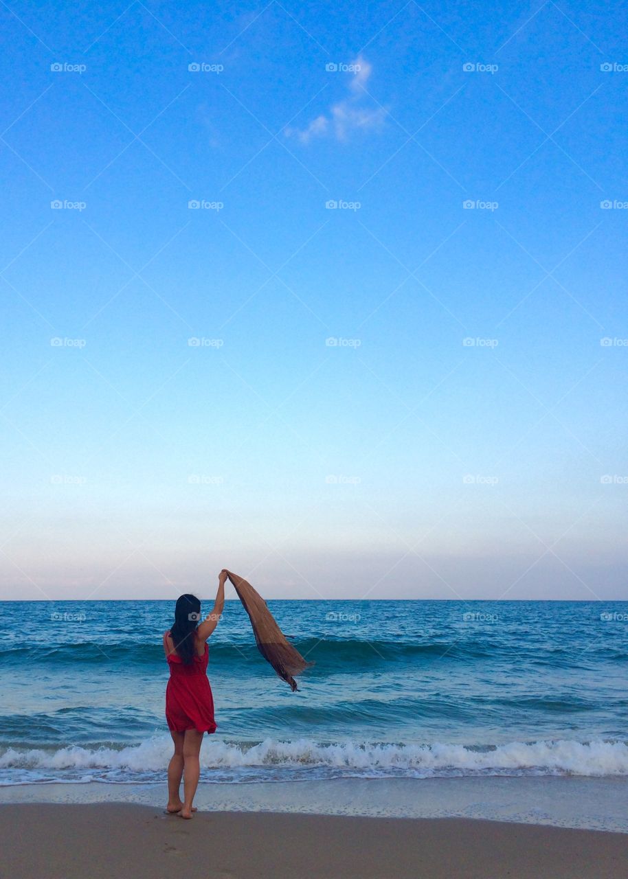 Young woman standing at the beach, waving her scarf in the air
