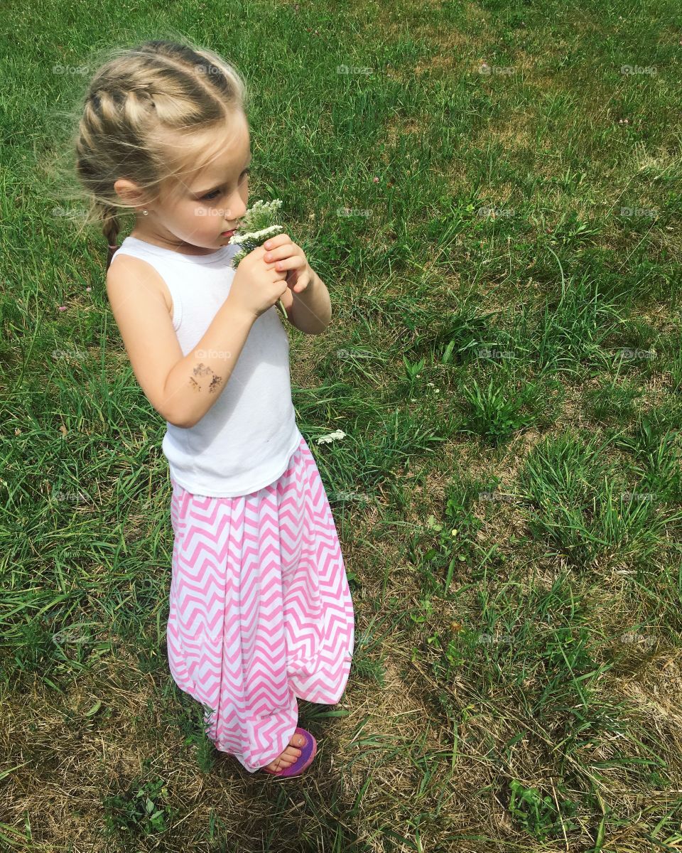 Little girl smelling flower standing on grass