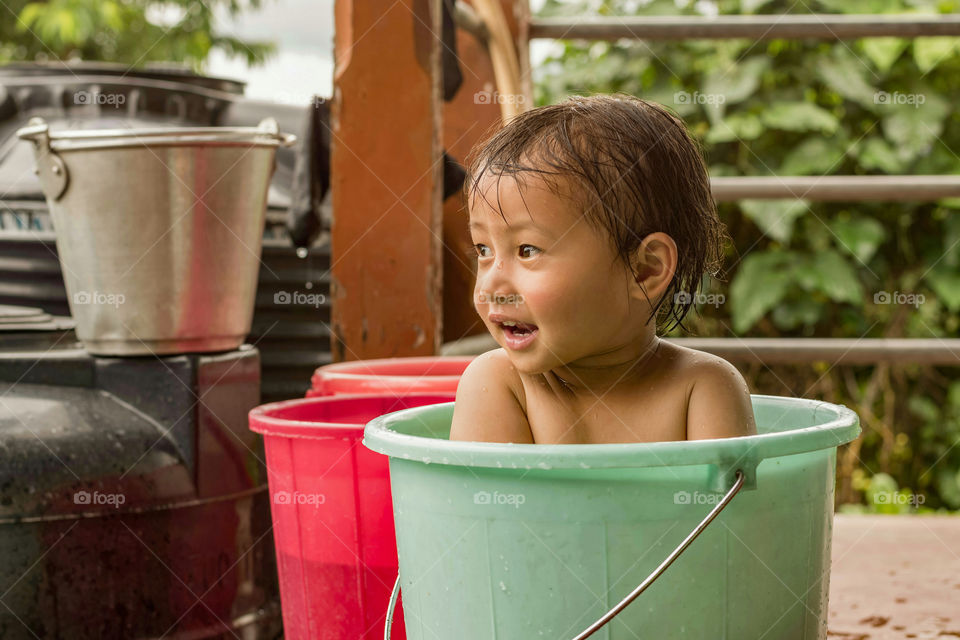 A little kid in a bucket enjoying an outdoor bath.