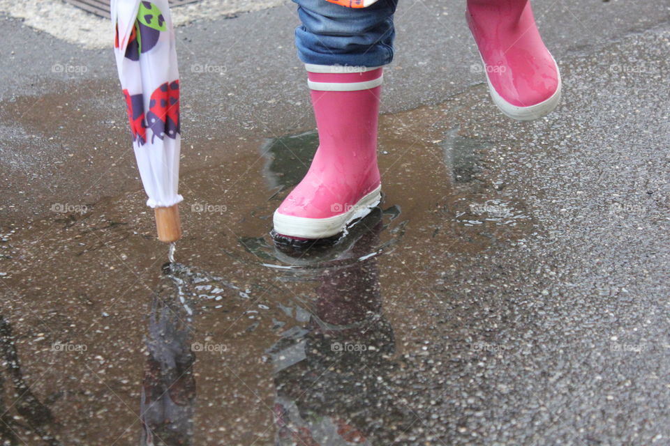 Two years old girl wears waterproof cape, umbrella and wellingtons