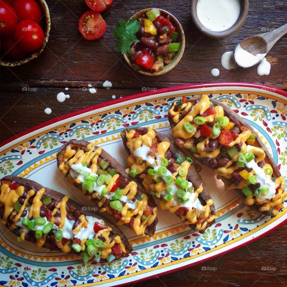Mexican stuffed sweet potatoes with vegan cheese and sour cream in a festive plate.