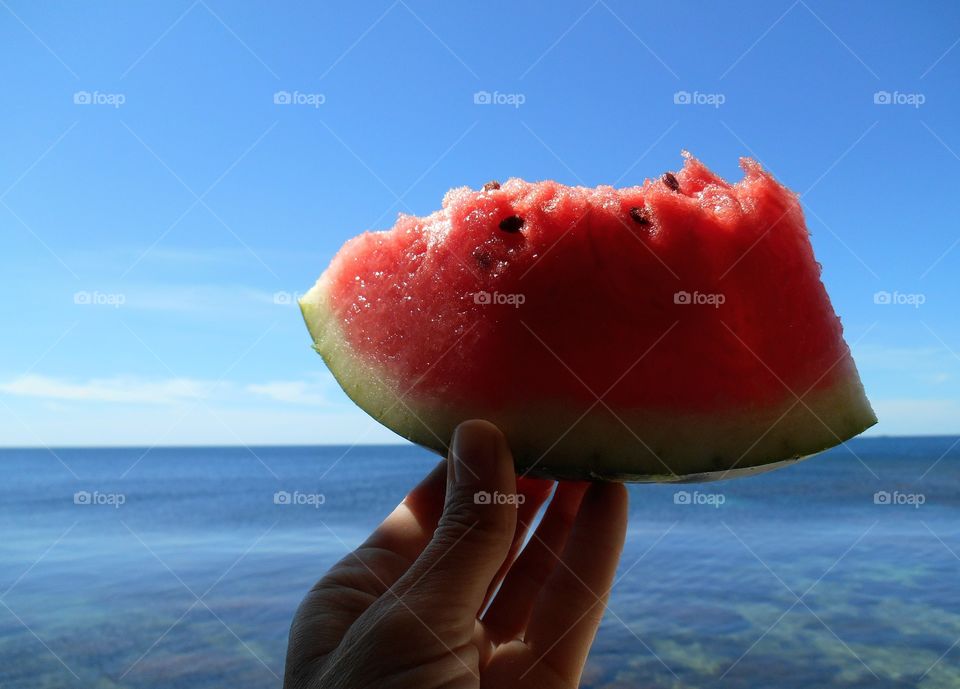 watermelon in the hand on a sea summer time blue sky background