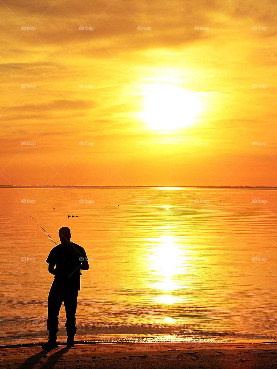 A silhouette of a angler tries his luck at fishing during a brilliant, golden sunset