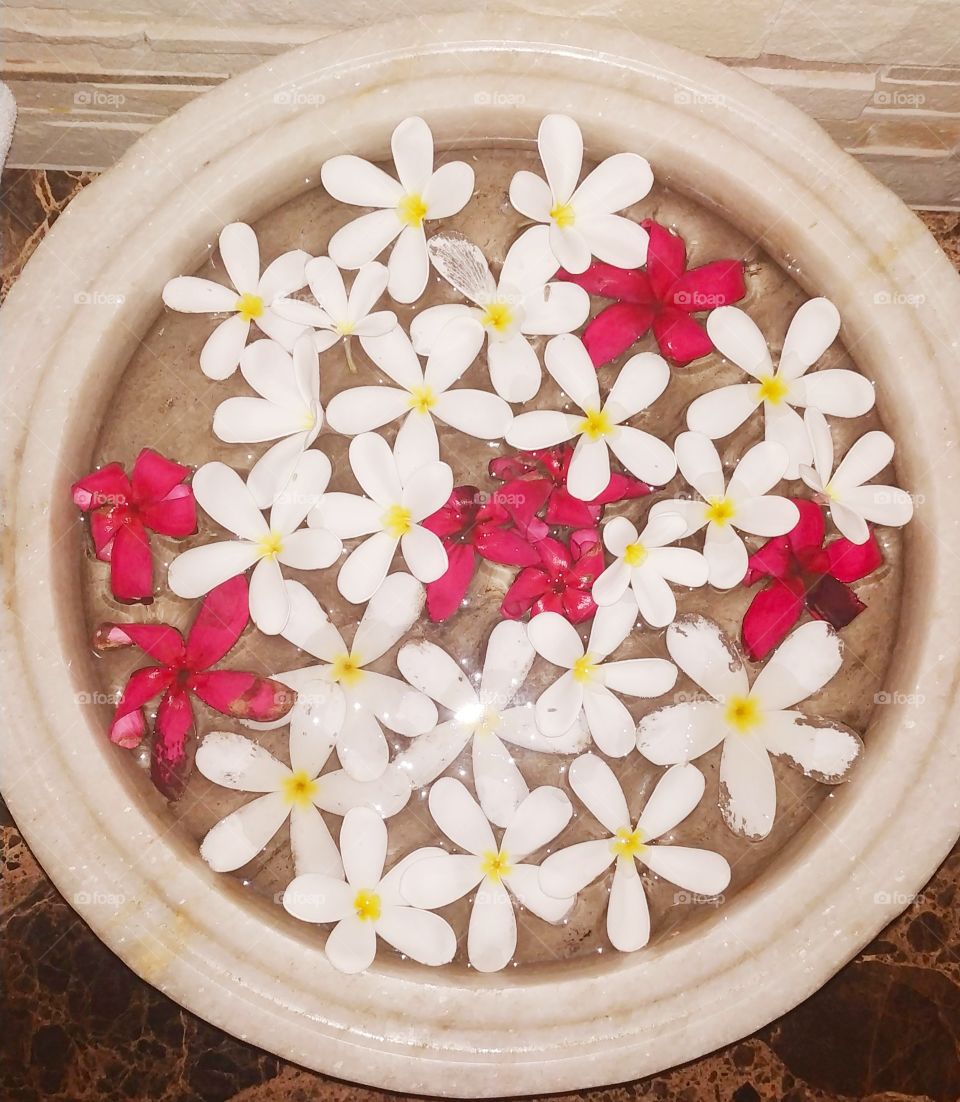 It is a stone vessel which is of white color and is filled with water and red color and white colored flowers are also added to it.