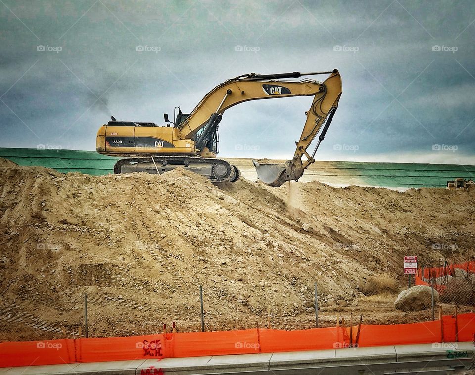 An Earth Excavator scoops up soil at a roadside grading project.