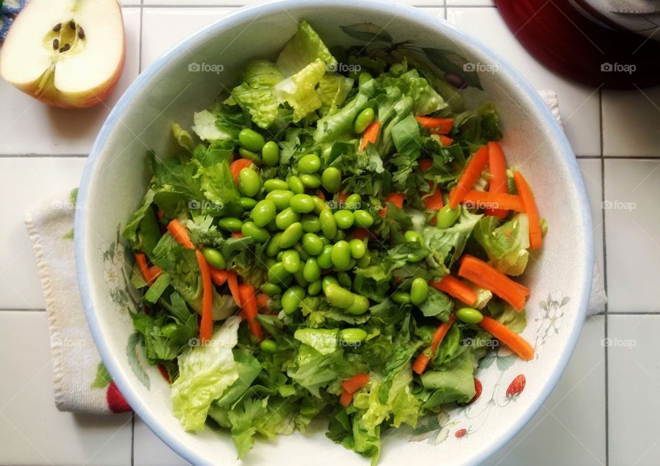 A large bowl of green salad with apple edamame peppers carrots