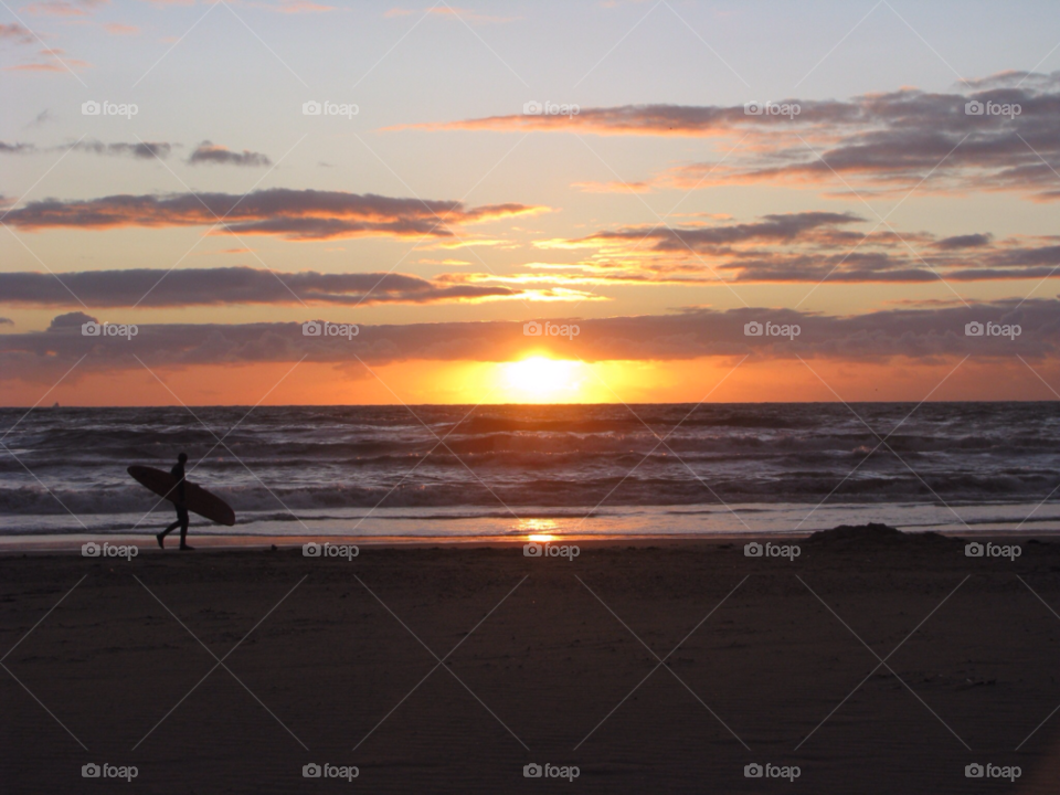 Surfer at sunset. Surfer carries surfboard at sunset at the beach 