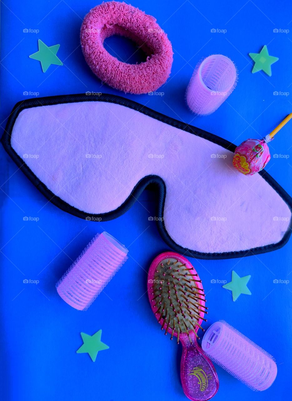 Barbie style.  On a dark blue background are: a pink eye mask, pink curlers, "Chupa Chyps", pink hair comb and stars,