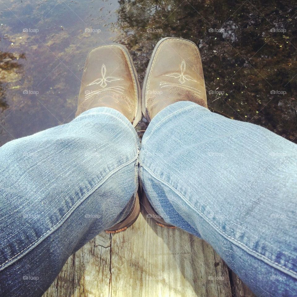 Dirty boots and jeans hanging over the lakes dock