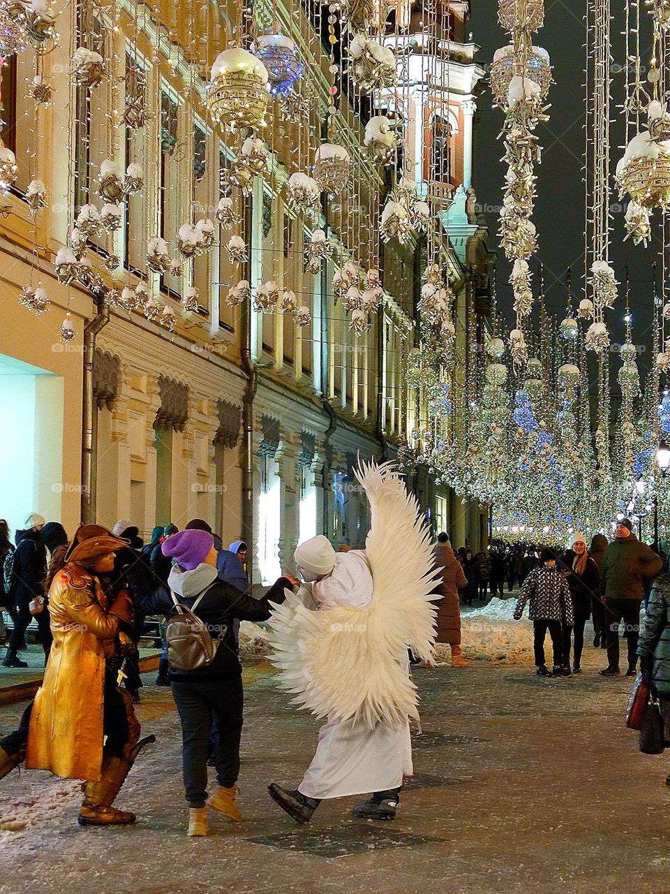Happiness. On a winter evening street that glows from burning garlands, a man dressed as a pirate and a man dressed as an angel are dancing with a girl. Photo from which the beholder has a smile on his face and happy emotions